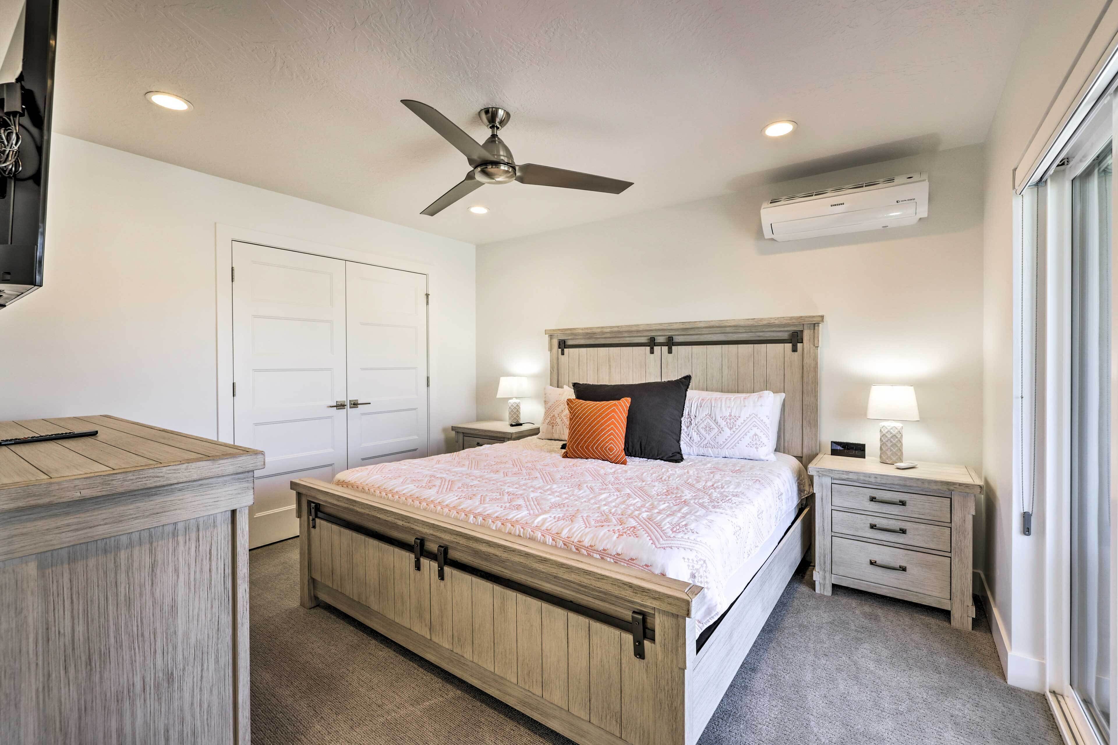 A bedroom with a wooden bed, bedside tables, a ceiling fan, an air conditioner, and a sliding door.