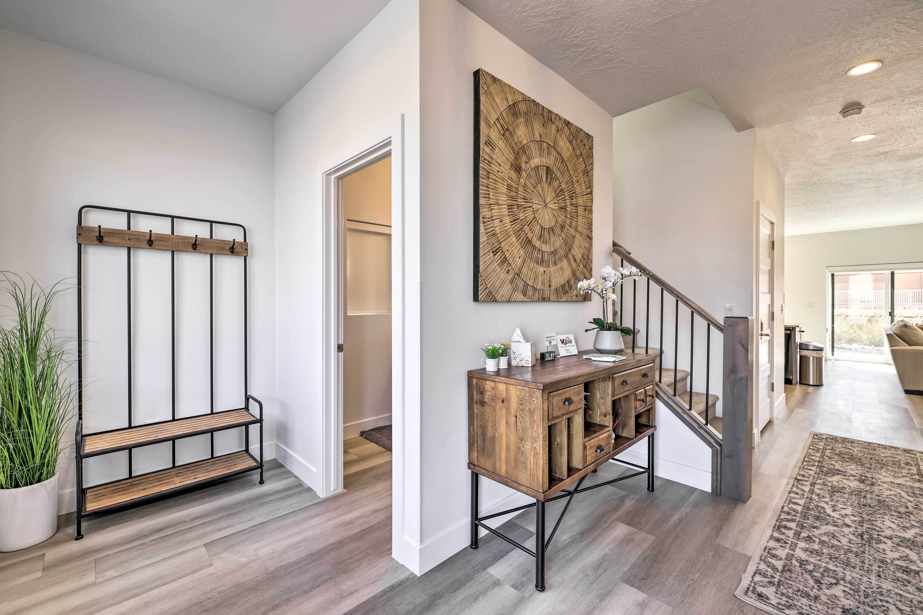 A modern interior with a wooden bench, a decorative wall piece, a staircase, and a console table with various items.