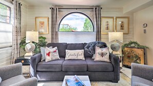 A living room with a dark grey sofa, two armchairs, a coffee table, and a large window with curtains. There are framed pictures on the walls and a decorative lamp on a side table. - Lovely Green Valley Abode w/ Community Pool! (Green Valley)