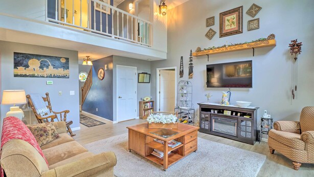A spacious living room with a high ceiling, a balcony, a fireplace, and a large TV.