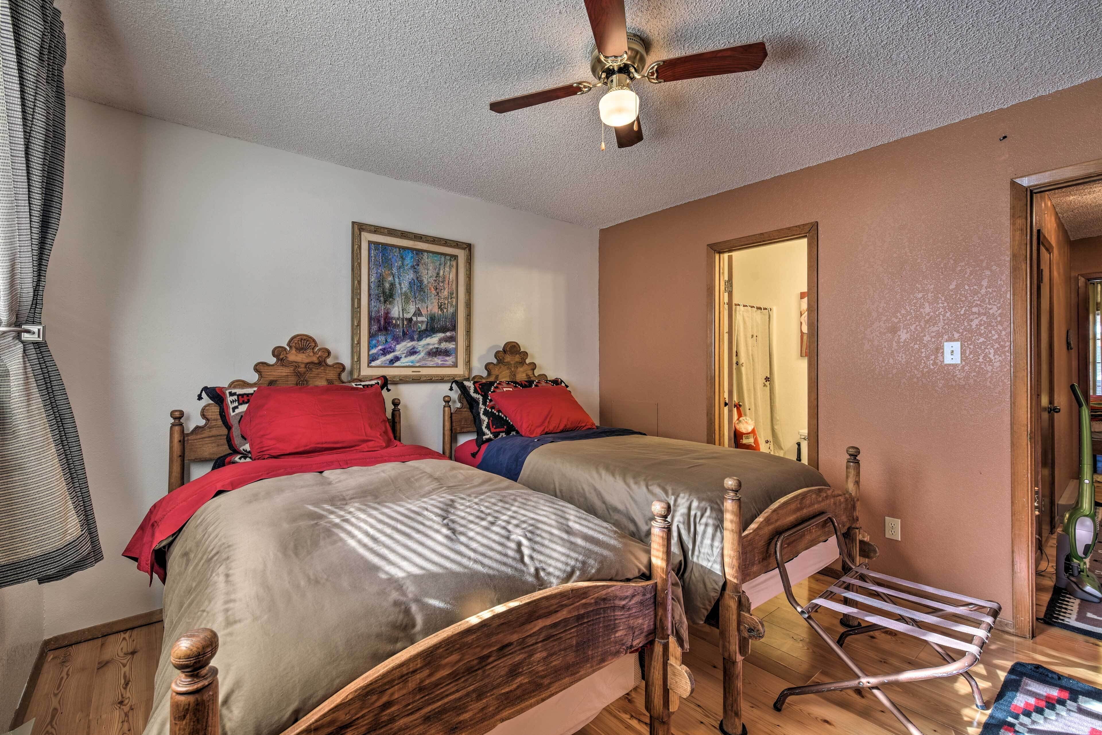 A bedroom with two beds, a ceiling fan, a painting, and a door leading to another room.