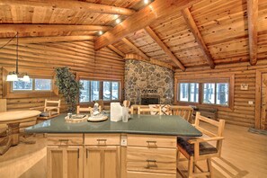 A log cabin interior with a stone fireplace, wooden furniture, and large windows. - 11 Mi to Rainbow Lake: Family Home w/ Large Yard (Pinetop)