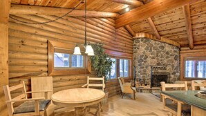 A log cabin interior with a stone fireplace, wooden furniture, and large windows. - 11 Mi to Rainbow Lake: Family Home w/ Large Yard (Pinetop)
