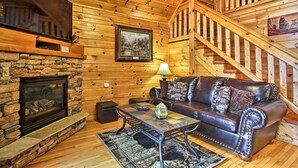 A cozy log cabin interior with a stone fireplace, leather sofa, and a wooden staircase. - Game Room & Hot Tub! Black Bear Falls Resort Cabin (Gatlinburg)