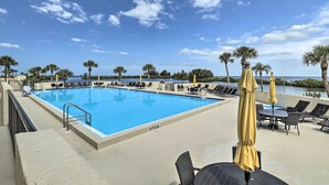 A swimming pool with lounge chairs and umbrellas, surrounded by palm trees and a view of the water. - Modern Waterfront Hudson Condo w/ Resort Pool! (Hudson)