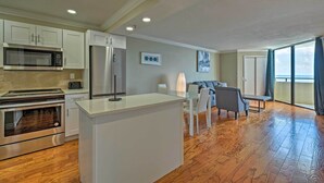 A modern kitchen with white cabinets, a built-in microwave, and an oven. There is a dining area with a table and chairs, and a large window with curtains. - Modern Waterfront Hudson Condo w/ Resort Pool! (Hudson)