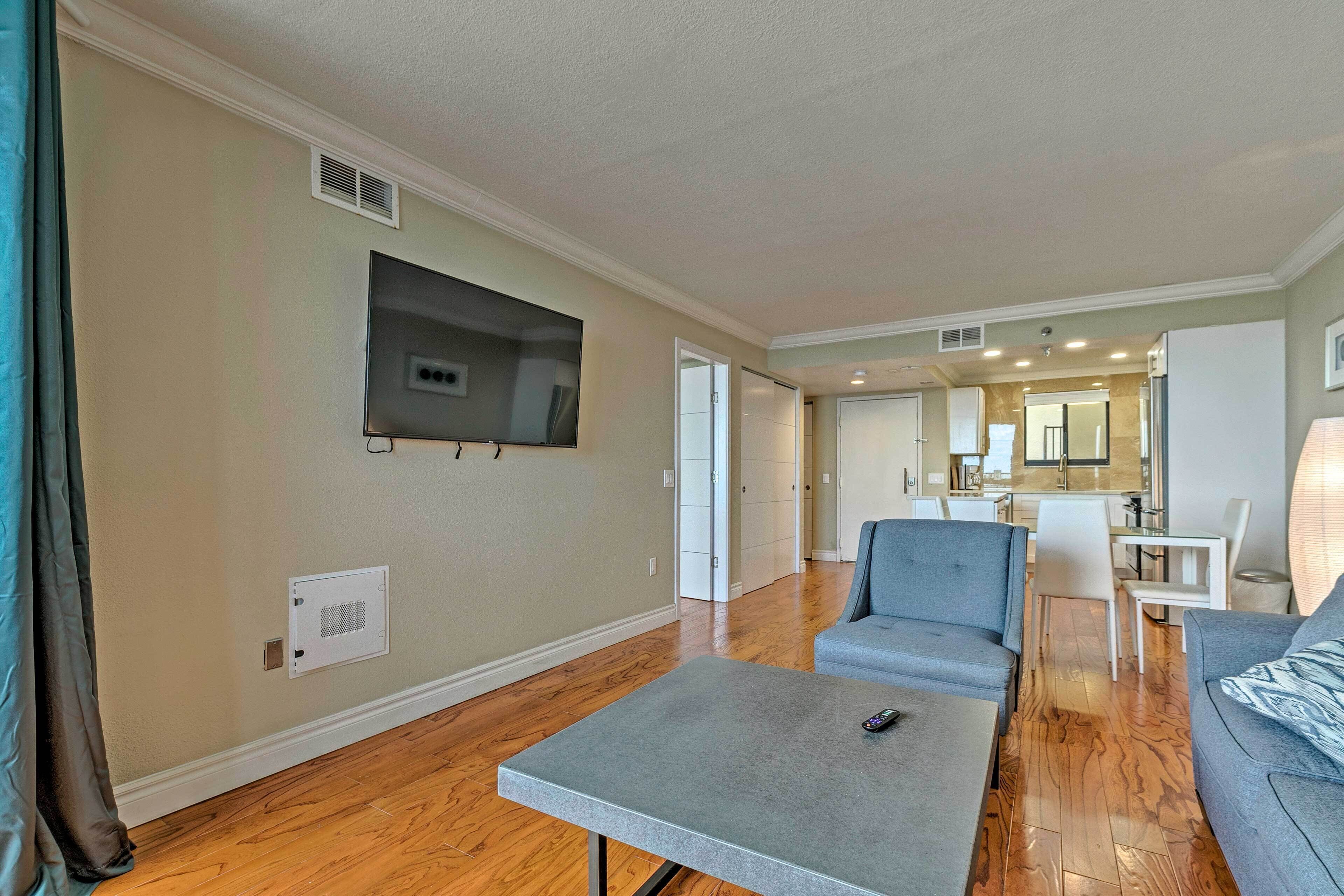 A spacious living room with a flat-screen TV mounted on the wall, a grey coffee table, and a grey sofa.