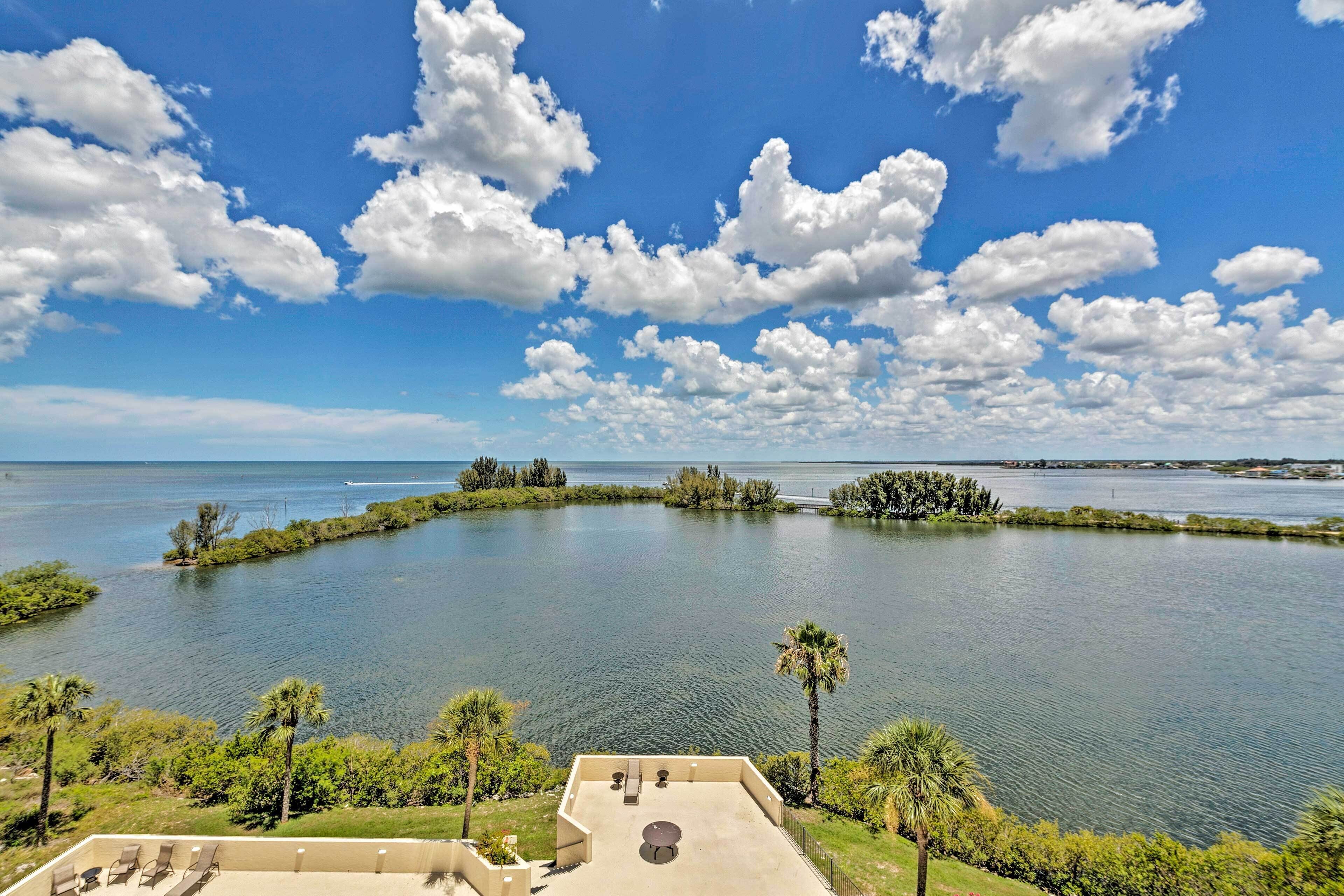 A view of a lake with a clear sky and clouds, surrounded by greenery and palm trees.