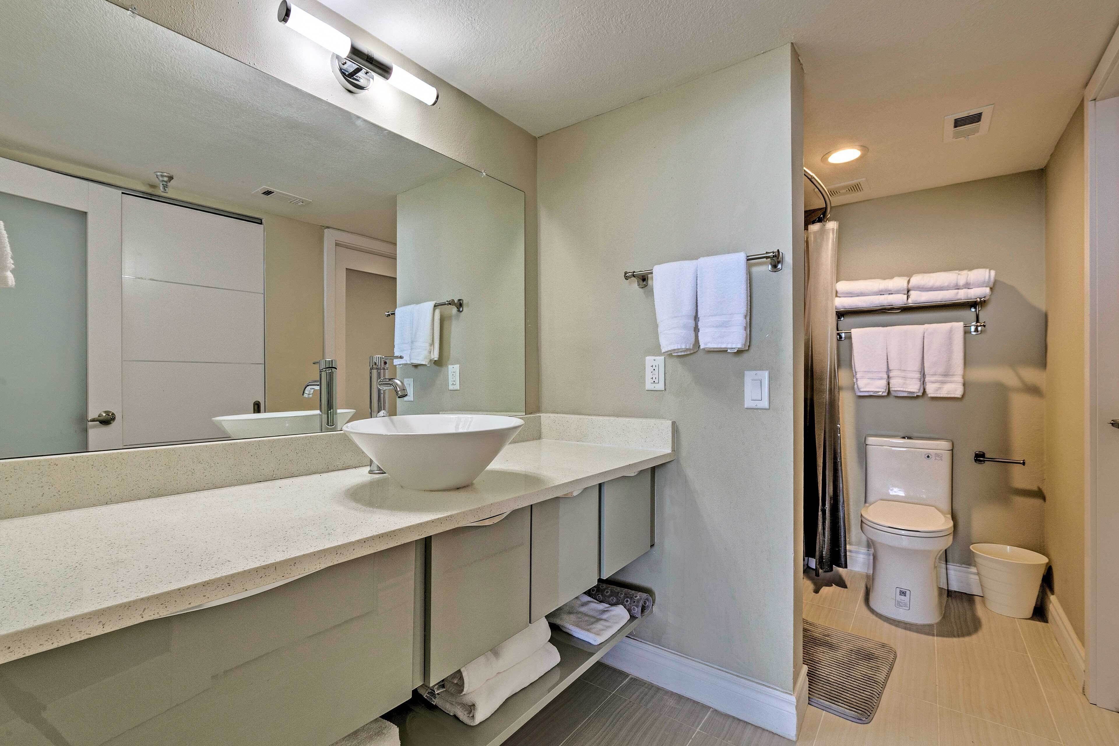 A modern bathroom with a large mirror, a vessel sink, a toilet, and a shower area.