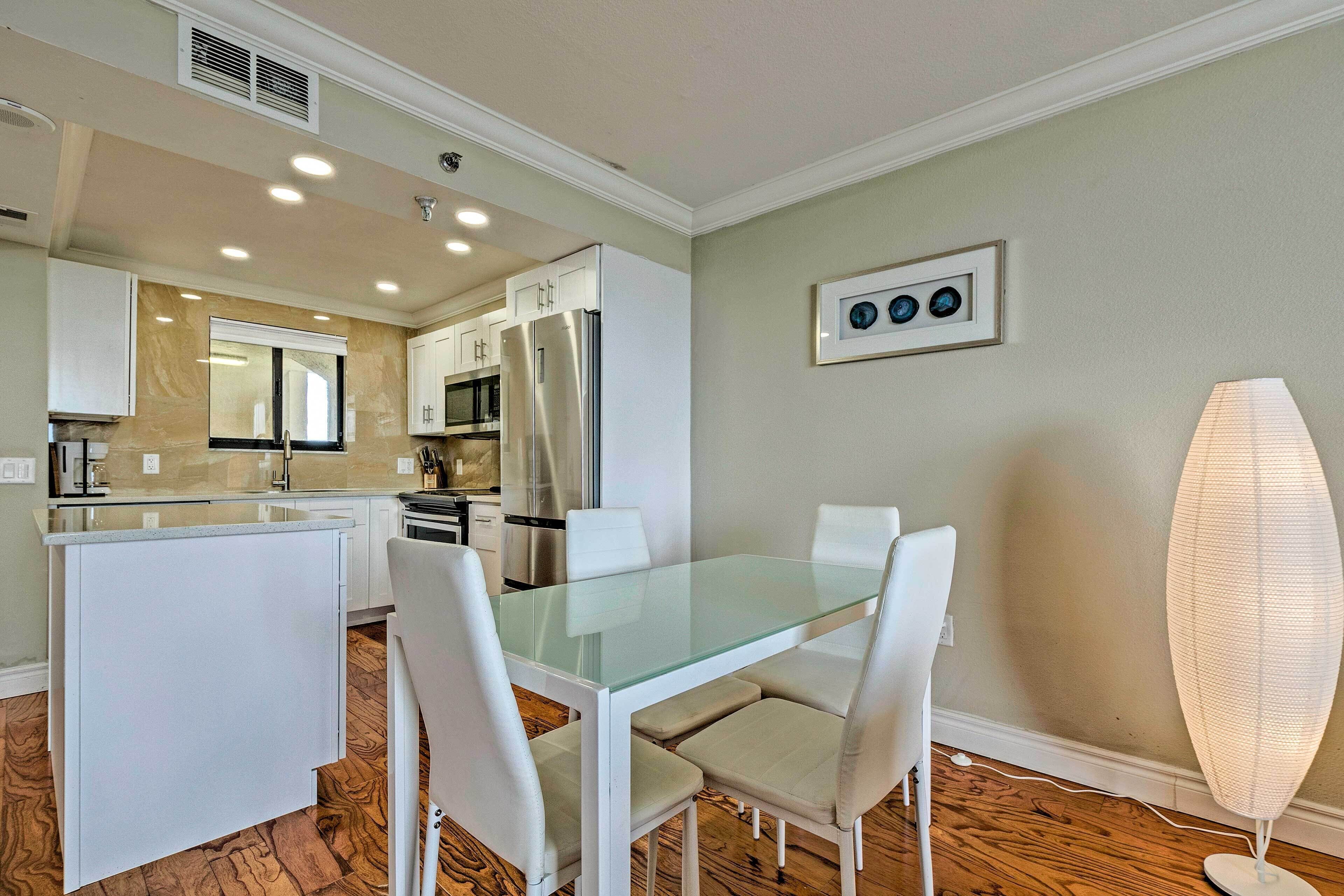 A modern kitchen with white cabinets, a glass dining table, and a white island.
