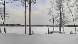 A snowy landscape with a wooden deck and a lamp post. - Lakefront Cabin w/ Private Dock & Beach! (Manistique)