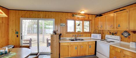 Cocina de cabaña de madera con una mesa de comedor, sillas, estufa y pileta.