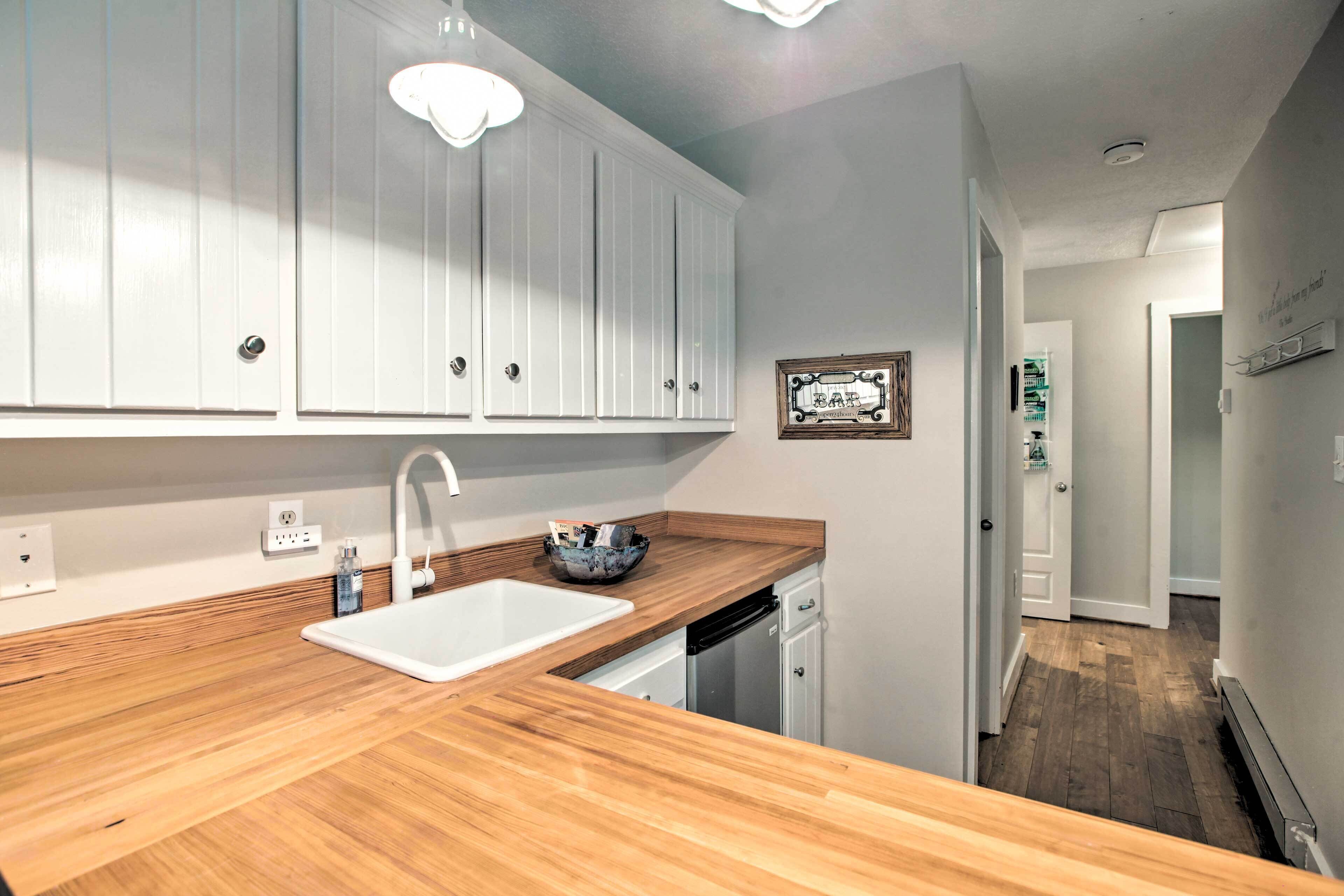 Una cocina con armarios blancos, encimera de madera, un lavabo y un refrigerador.