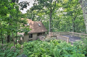 A house surrounded by dense greenery, with a wooden deck and a staircase leading to a porch.