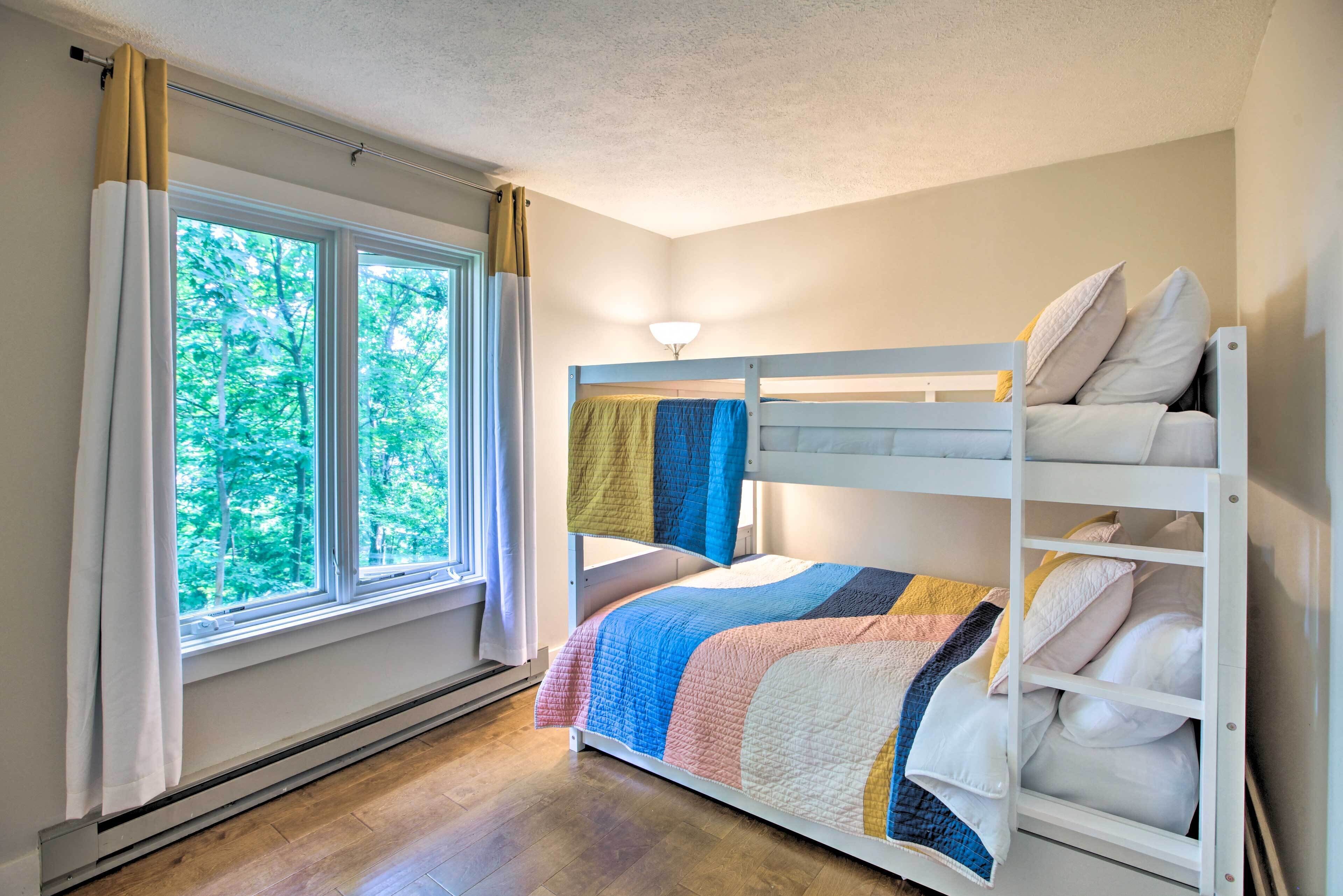 A bunk bed with a colorful quilt, a window with curtains, and a ceiling light.