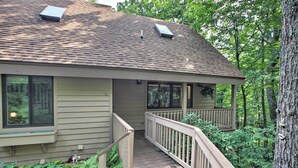 A house with a covered porch, a wooden deck, and a view of the surrounding forest.