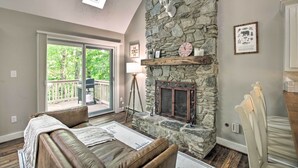 A cozy living room with a stone fireplace, a leather sofa, and a large sliding glass door leading to a balcony.