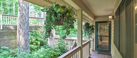 A covered porch with a hanging plant, wooden railing, and a door leading to a garden area.