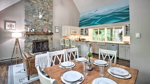 A dining area with a stone fireplace, white chairs, and a wooden table set for four.