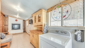 A laundry room with a washing machine, wooden cabinets, a fireplace, and a window with blinds. - Ruidoso Cabin - Walk to Local Park + Downtown (Ruidoso)