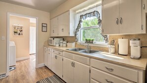 A modern kitchen with white cabinets, a double sink, a coffee maker, and a window with a decorative curtain. - Home w/ Fenced Yard by 5 Mighty Nat'l Parks (Circleville)