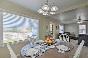 A dining area with a table set for four, a fruit bowl, and a view of the outside through large windows.