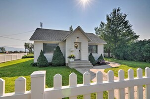 A single-story house with a front porch, a small garden with two potted plants, and a white picket fence.