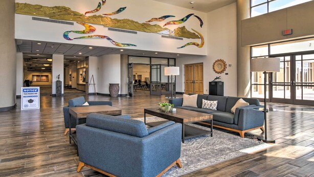 Um hall amplo com design moderno, apresentando uma grande área de estar com sofás e uma mesa de centro, um mural decorativo no teto e uma janela grande que proporciona iluminação natural.