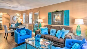 Sala de estar com um sofá azul, uma mesa de centro de vidro e um sofá marrom. Há luminárias decorativas, um espelho e um quadro na parede.