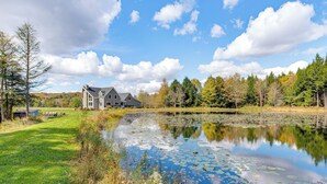 A large house with a pond in front, surrounded by trees and a clear sky. - Spacious & Secluded Forksville Home: Fire Pit (Forksville)