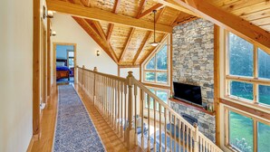 A spacious interior with a wooden staircase, stone fireplace, and large windows offering a view of the outdoors. - Spacious & Secluded Forksville Home: Fire Pit (Forksville)