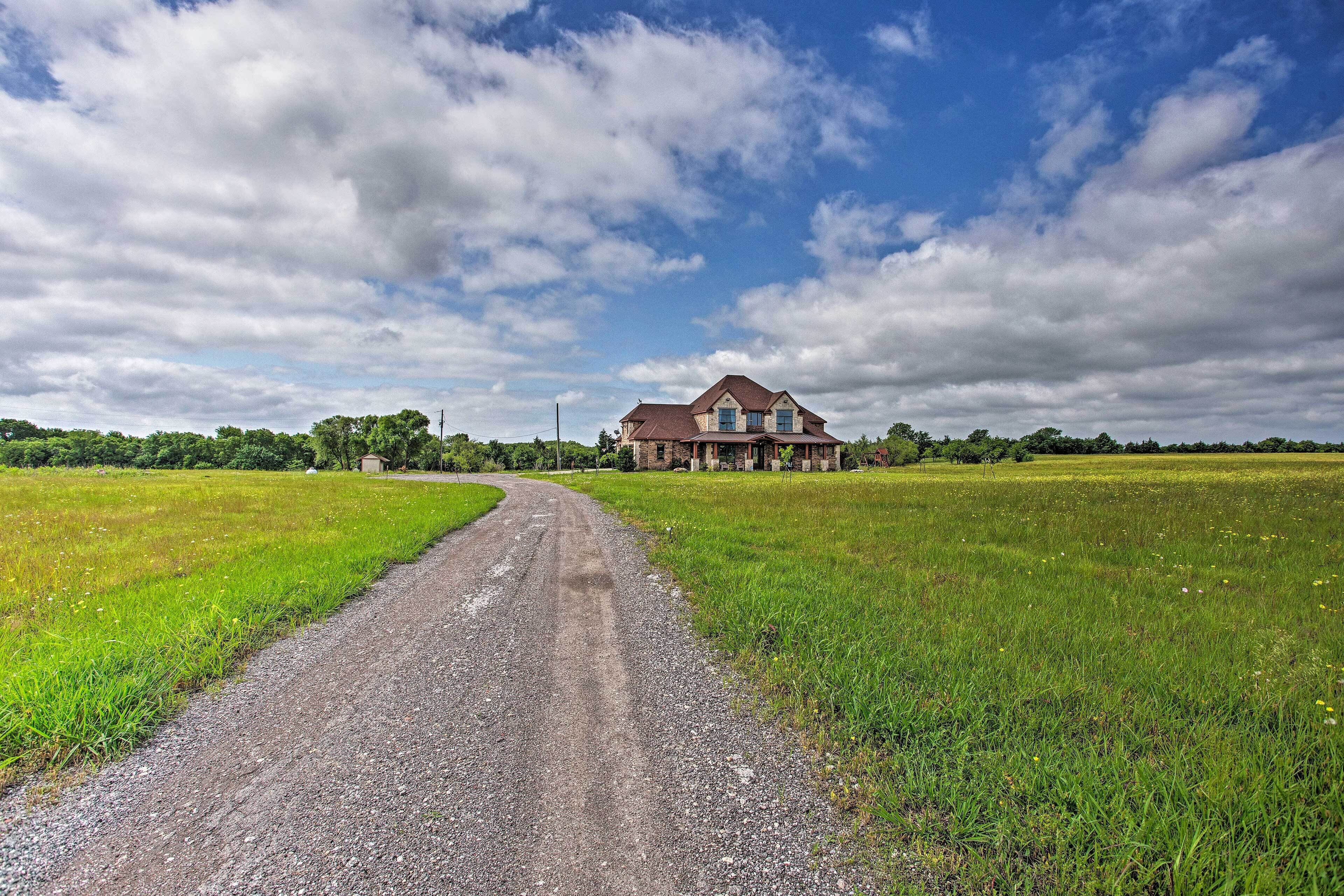 A rural road leading to a large house surrounded by fields.