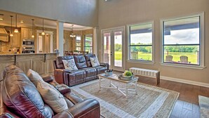 A spacious living room with a leather sofa, a coffee table, and large windows offering a view of the outdoors. - Home w/ Game Room & Fireplace: 14 Mi to Mckinney! (Blue Ridge)