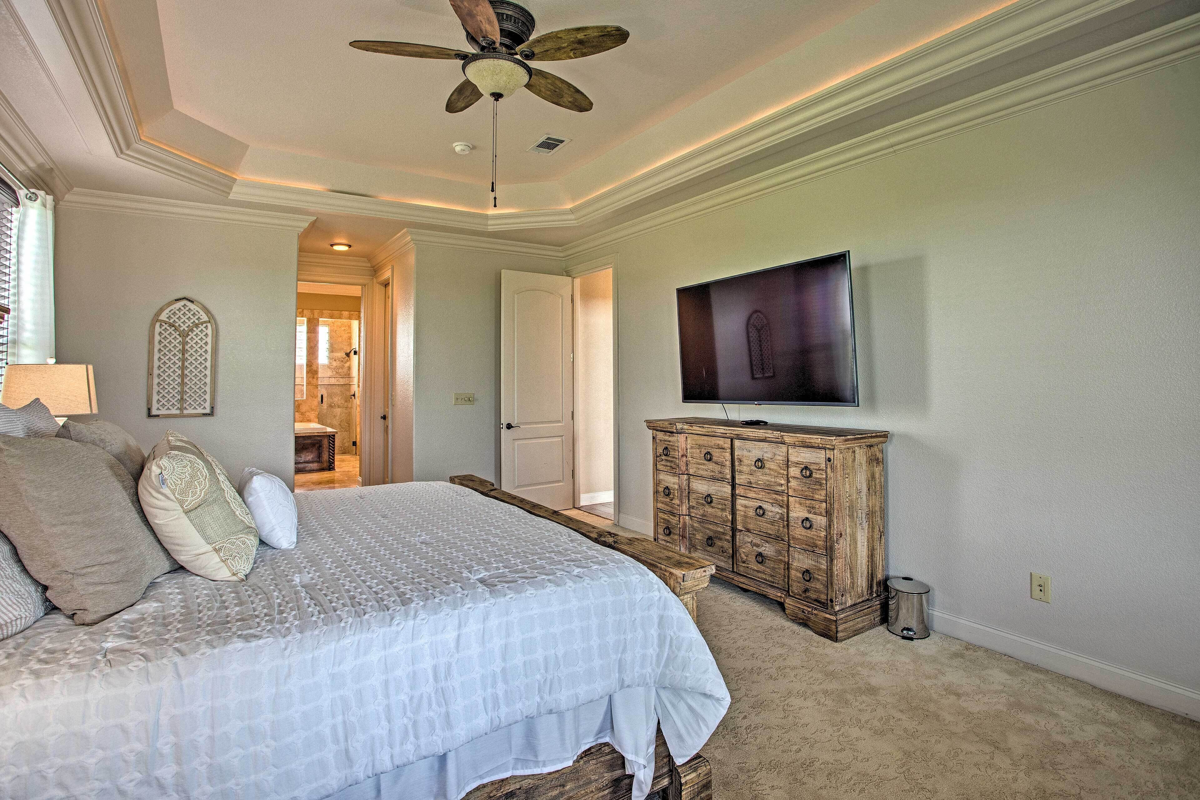 A bedroom with a bed, a wooden dresser, a television, and a ceiling fan.