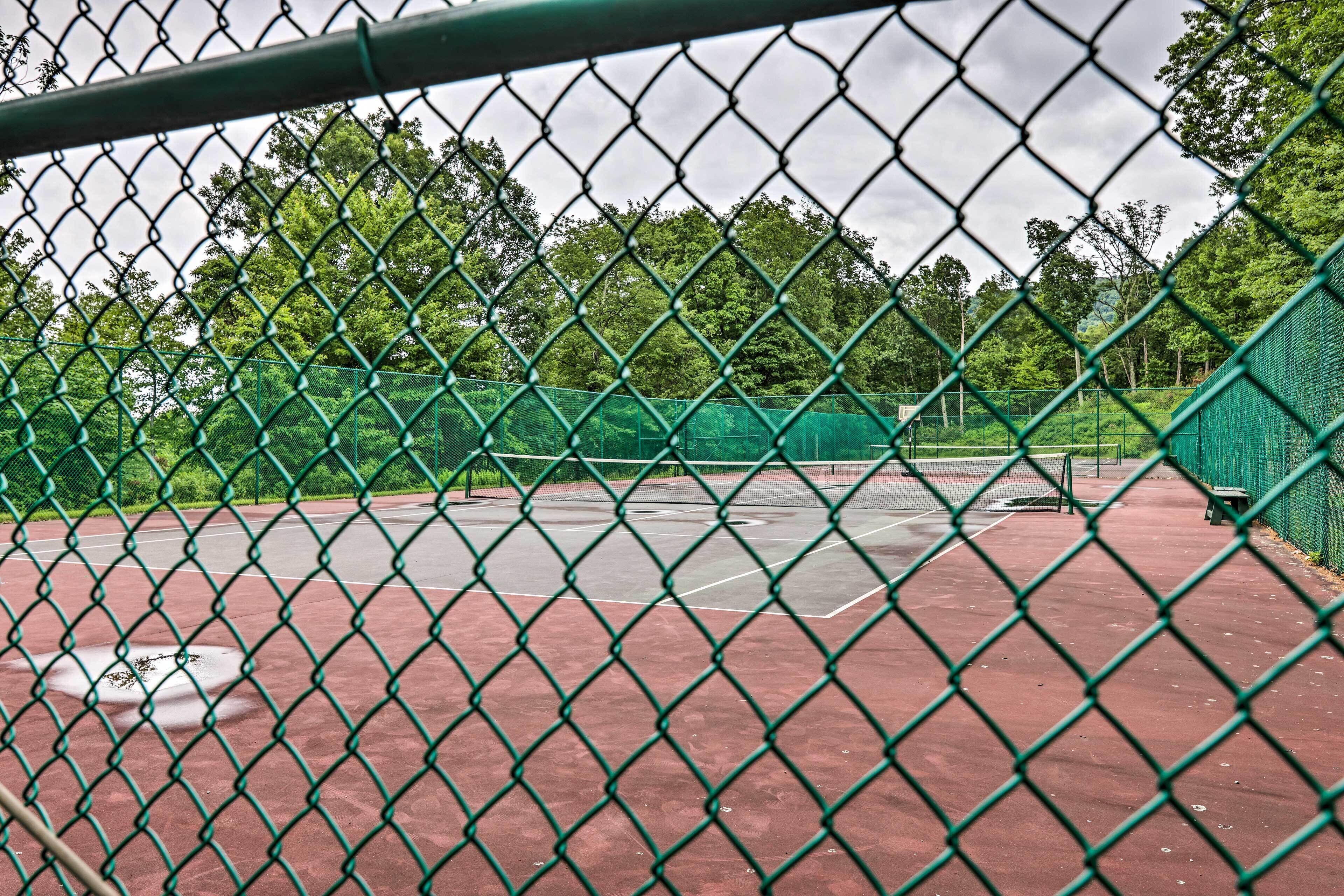 Una cancha de tenis con red, delimitada por una cerca de cadena y árboles al fondo.