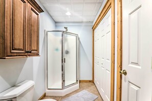 Un baño con inodoro, ducha con puerta de vidrio, armarios de madera y una puerta blanca.