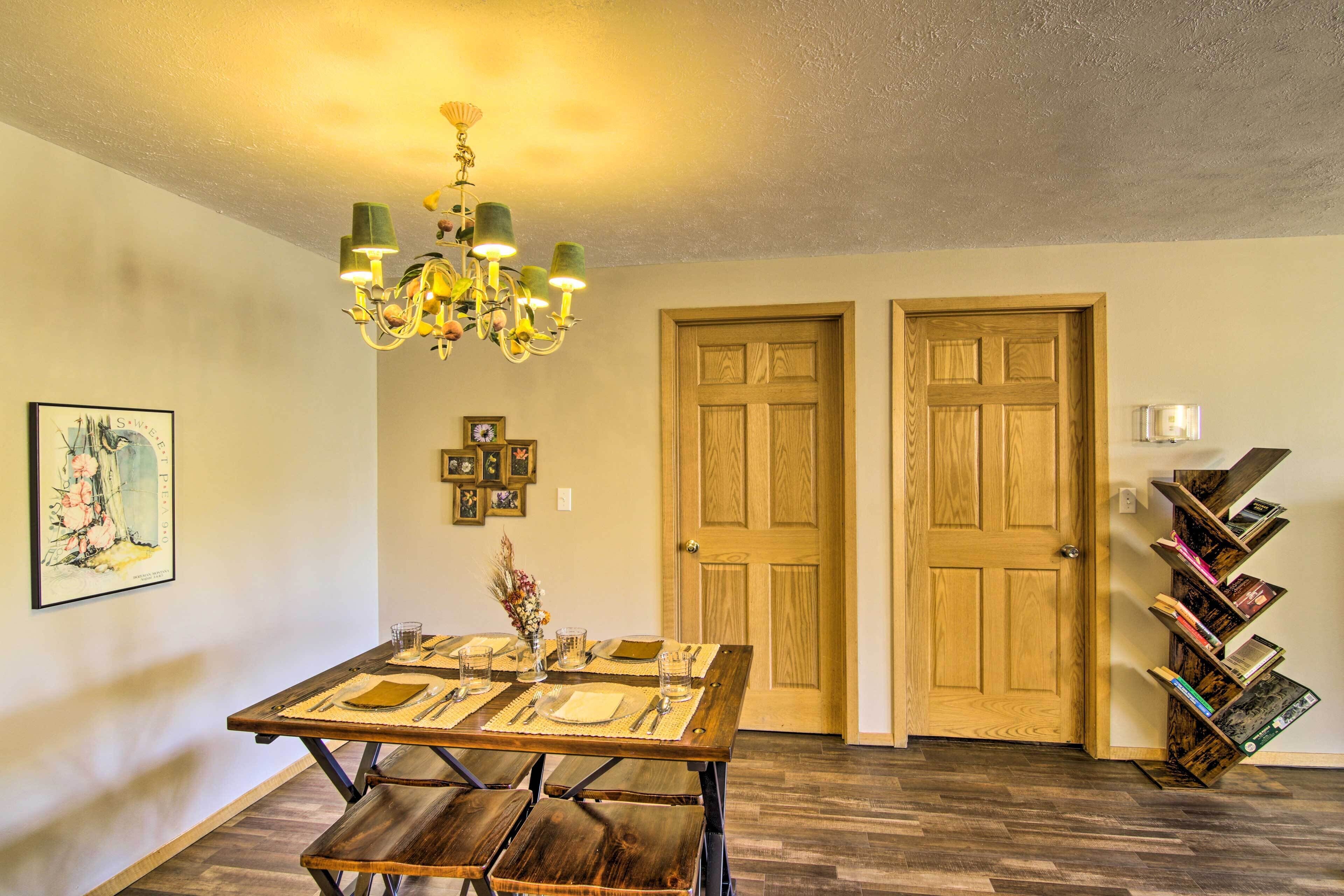 Uma área de refeições com uma mesa de madeira posta para quatro pessoas, um candelabro e duas portas de madeira.