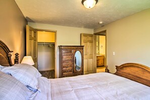 Ein Schlafzimmer mit einem großen Bett, einer Holzkommode mit Schubladen, einem Spiegel und einem Kleiderschrank mit Kleidung.
