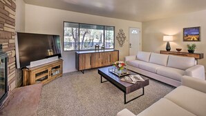 A modern living room with a flat-screen TV, a wooden entertainment unit, a beige sofa, a coffee table, and a large window offering a view of trees. - 'lakeside Traditions' Arizona Home w/ Game Room! (Lakeside)