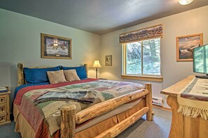 Um quarto aconchegante com estrutura de cama de madeira, uma janela grande com vista para árvores e uma escrivaninha com luminária.