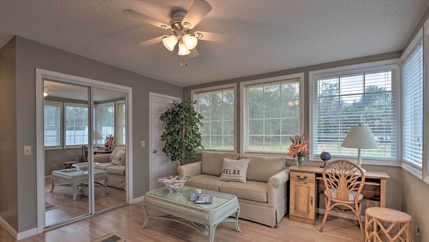 A living room with a glass coffee table, beige sofa, and a desk with a chair. - Hilton Head Waterfront Golf Getaway: Pet Friendly! (Hilton Head Island)