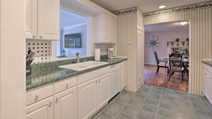 A kitchen with white cabinets, a granite countertop, and a dining area with a table and chairs. - Hilton Head Waterfront Golf Getaway: Pet Friendly! (Hilton Head Island)