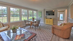 A spacious room with large windows, a dining table with chairs, a wicker sofa, and a flat-screen TV mounted on the wall. - Hilton Head Waterfront Golf Getaway: Pet Friendly! (Hilton Head Island)