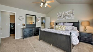 Ein Schlafzimmer mit Bett, Schminktisch, Nachttisch, Deckenventilator, Wanduhr und einem floralen Gemälde.