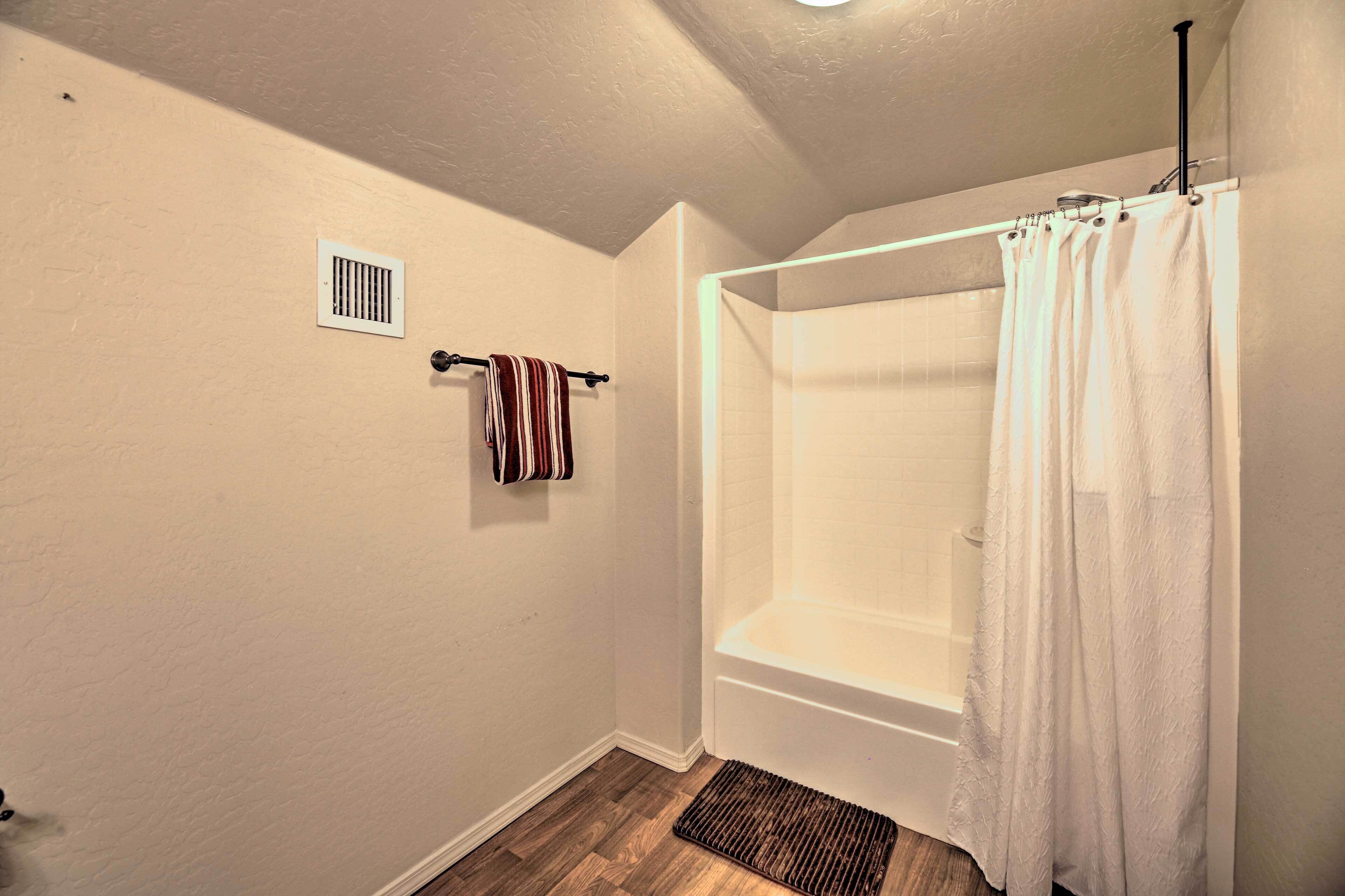Une salle de bain avec une baignoire, un rideau de douche, un porte-serviettes avec une serviette à rayures et une grille d’aération au mur.