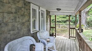 A covered porch with two wicker chairs, a stone wall, and a view of the surrounding greenery. - Enchanting Family House w/ Balcony < 3 Mi to Wvu! (Morgantown)