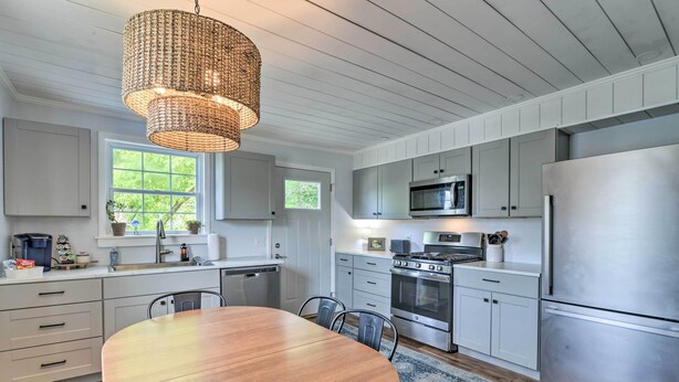 A modern kitchen with white cabinetry, stainless steel appliances, a wooden dining table, and a woven pendant light. - Enchanting Family House w/ Balcony < 3 Mi to Wvu! (Morgantown)