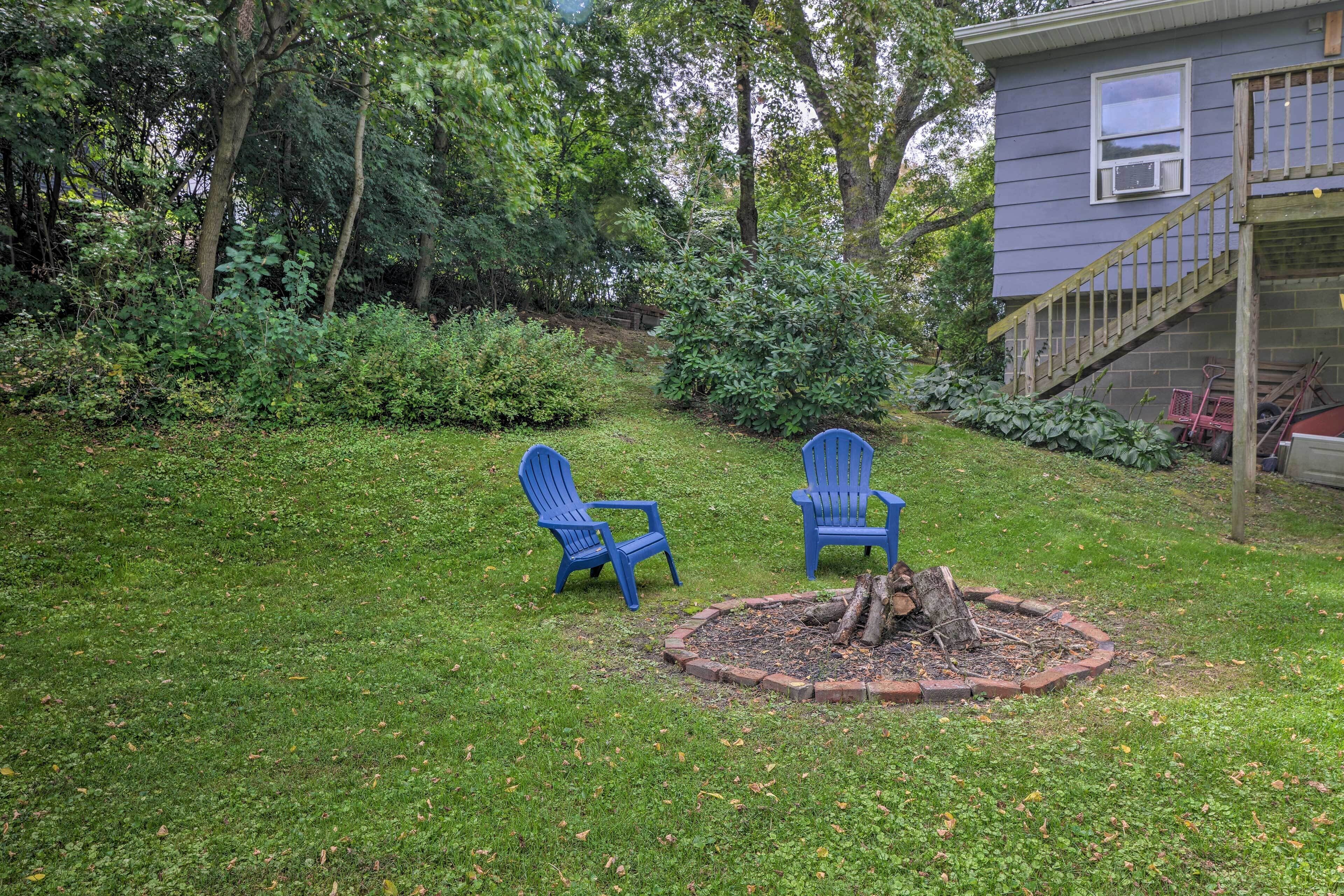 Ein Garten mit zwei blauen Adirondack-Stühlen, einer Feuerstelle und einem Haus mit einer Holztreppe.