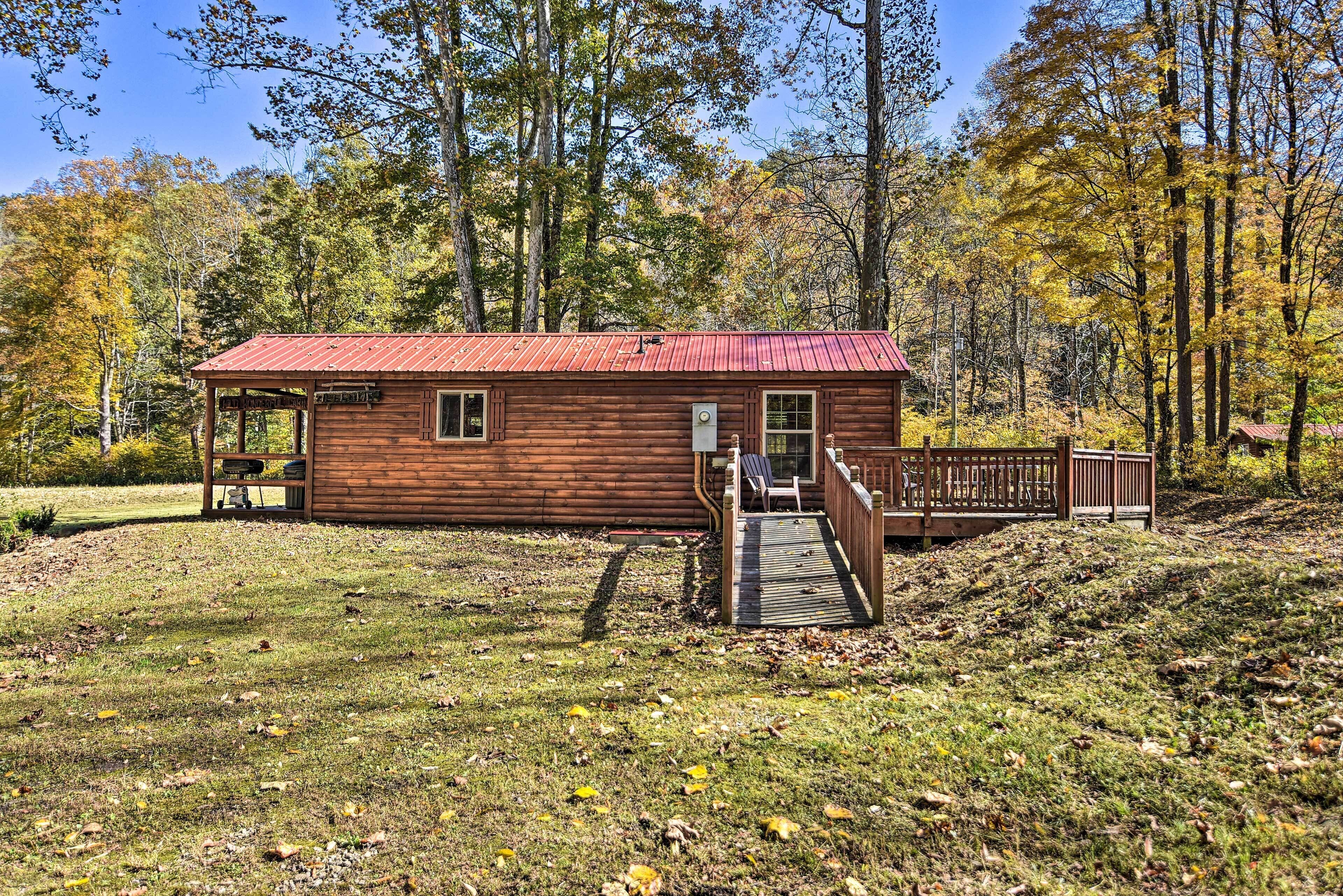 Une cabane en bois avec un toit rouge, une véranda couverte et une terrasse en bois menant à l’entrée.