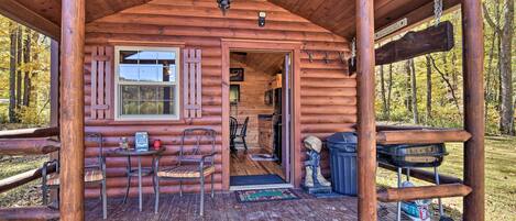 Une cabane en bois avec un porche, un coin repas avec des chaises, une petite table et un barbecue.